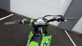 Green Kawasaki KX250X dirt bike parked outside a garage door.