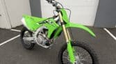 Green Kawasaki KX250X dirt bike parked outside near a garage door.