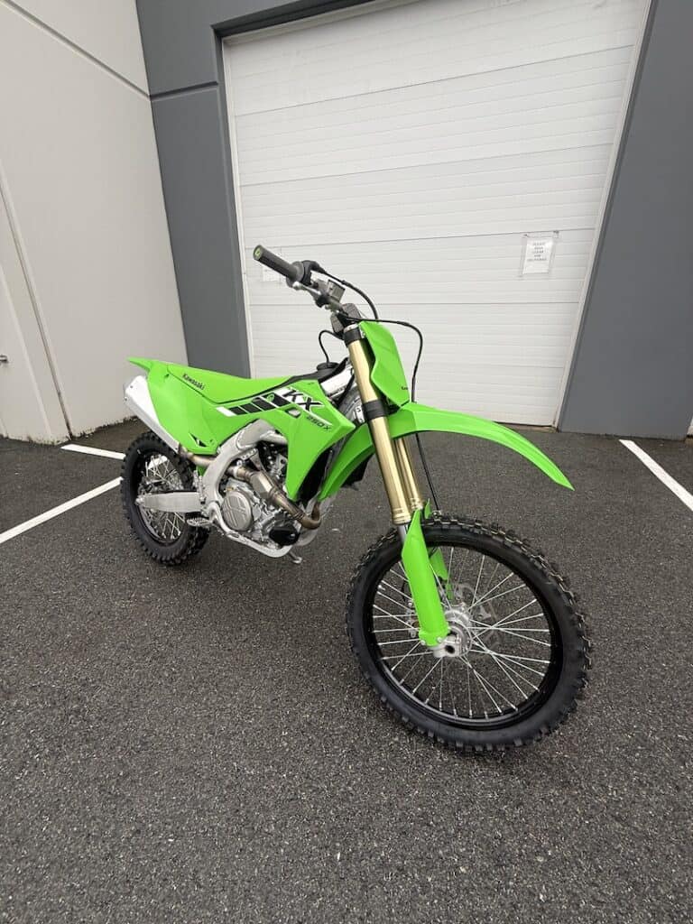 Green Kawasaki KX250X dirt bike parked outside near a garage door.
