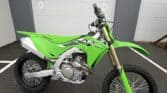 Green Kawasaki KX250X dirt bike parked outside with garage doors in background.